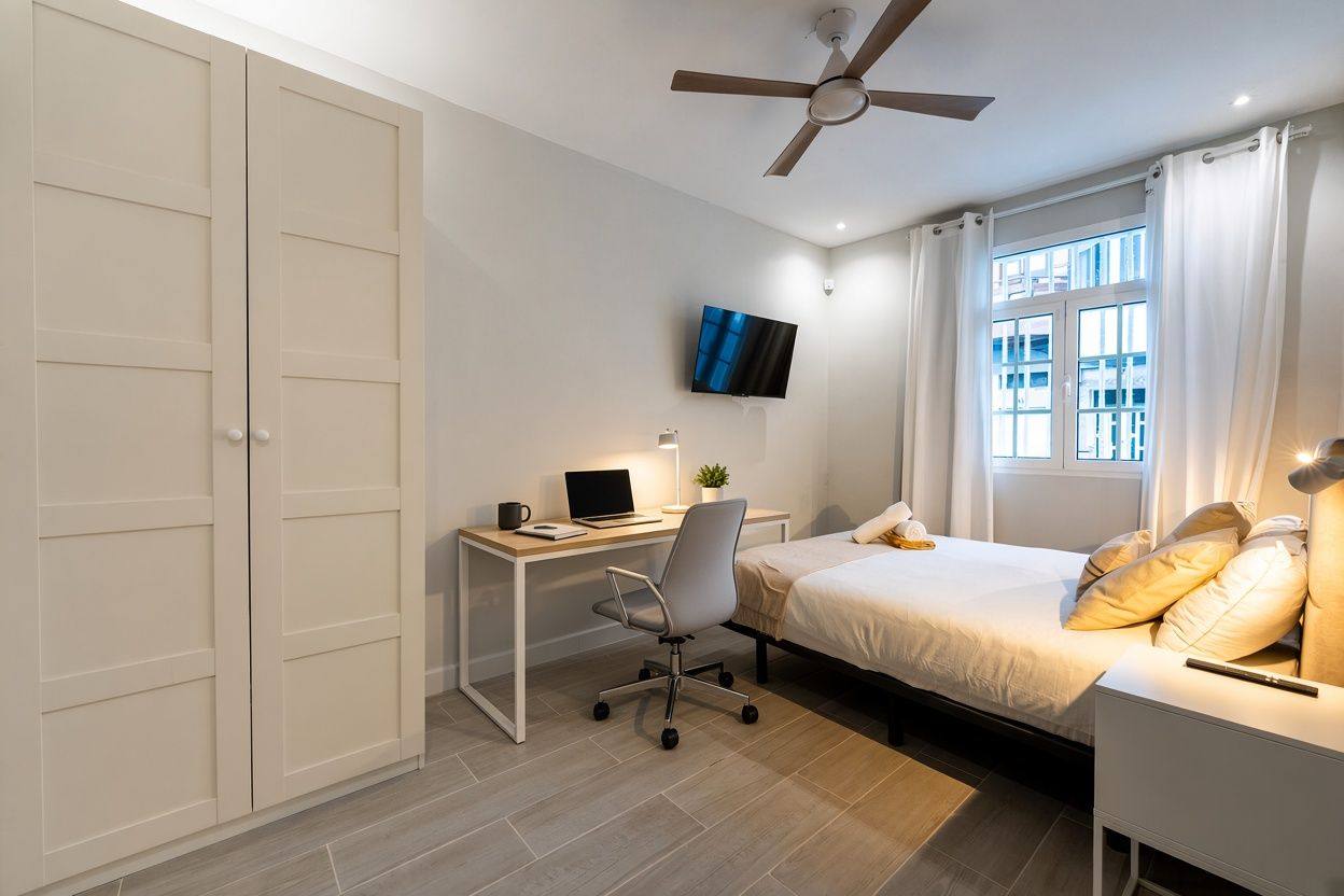 Bright double room with a white desk, office chair and laptop next to the window